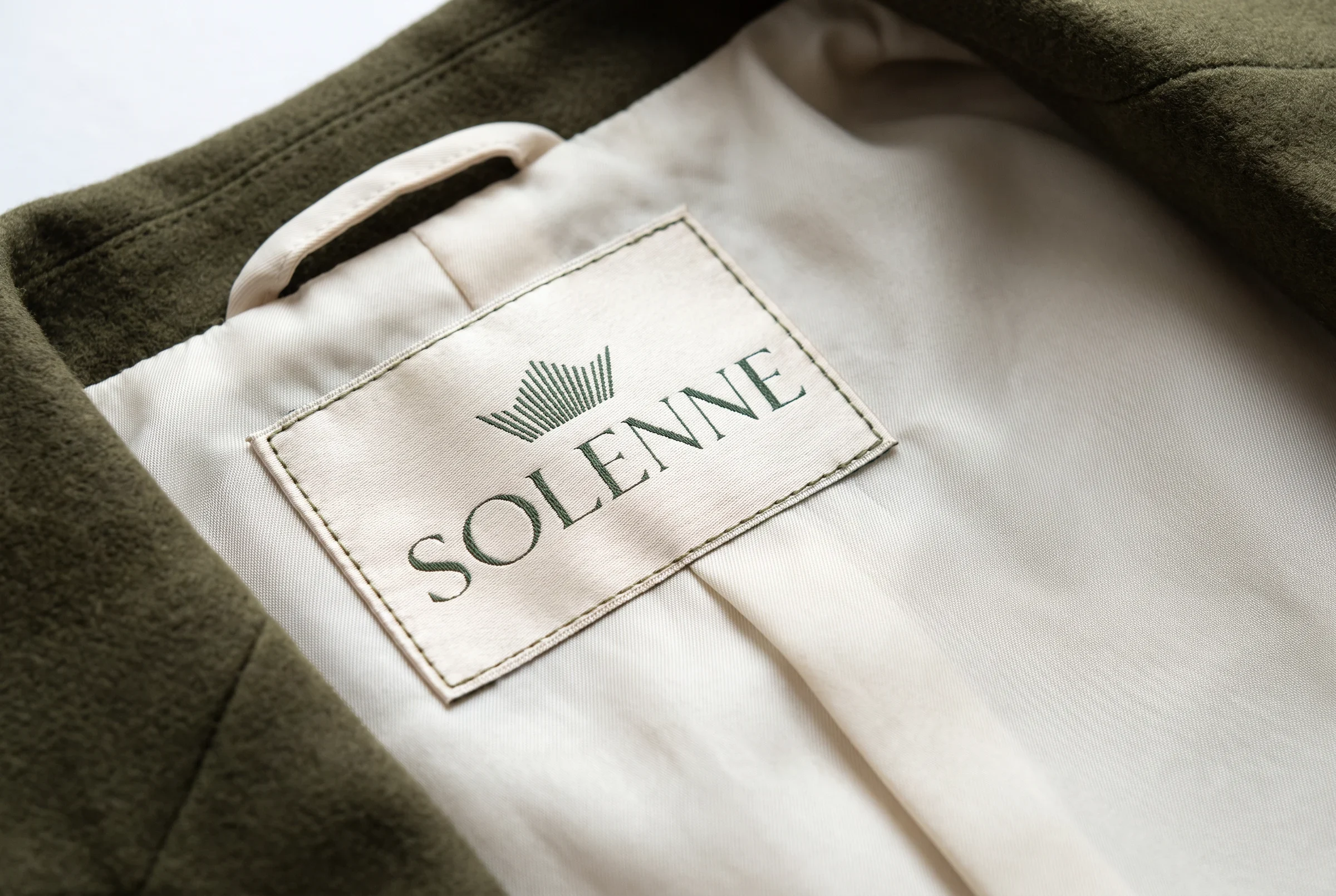 Woven Solenne label sewn inside an olive tailored coat.
