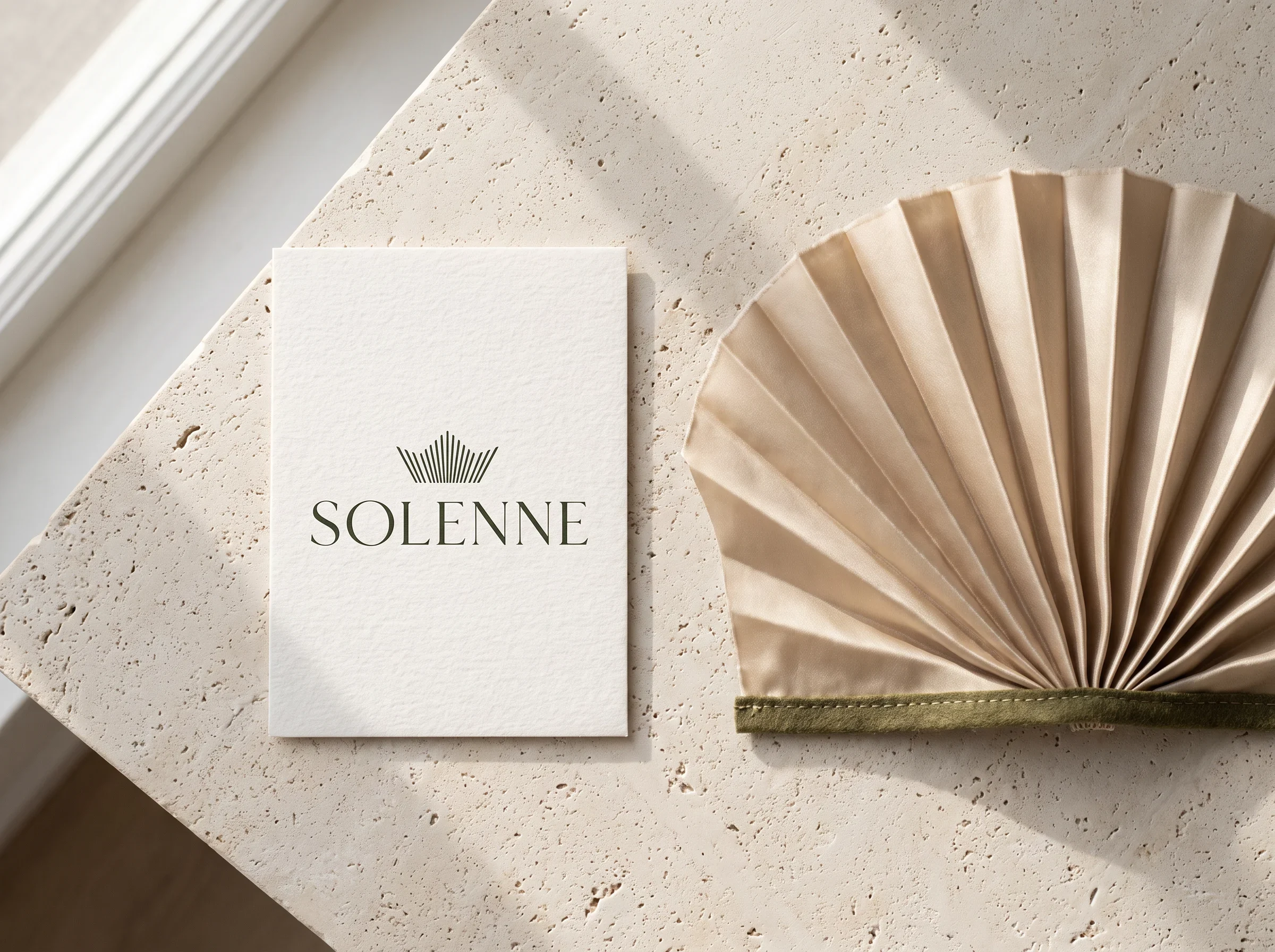 Solenne business card beside pleated champagne silk edged in olive.
