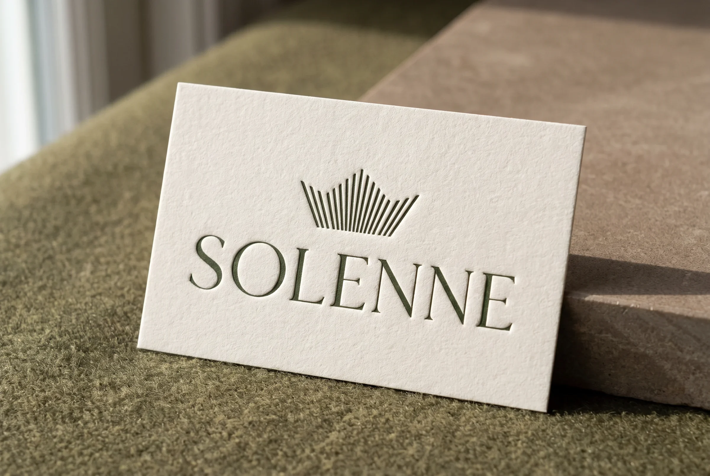 Embossed Solenne business card photographed on olive textile and warm stone.
